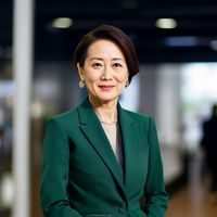 佐山爱创始人张梅女士的专业形象照，身着深绿色职业装，背景为品牌展厅，神情自信而亲切