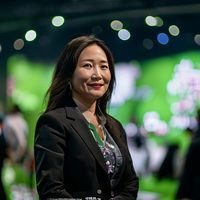 佐山爱品牌运营总监陈欣女士的专业照片，站在品牌活动现场，背景是充满绿意的布景和品牌LOGO